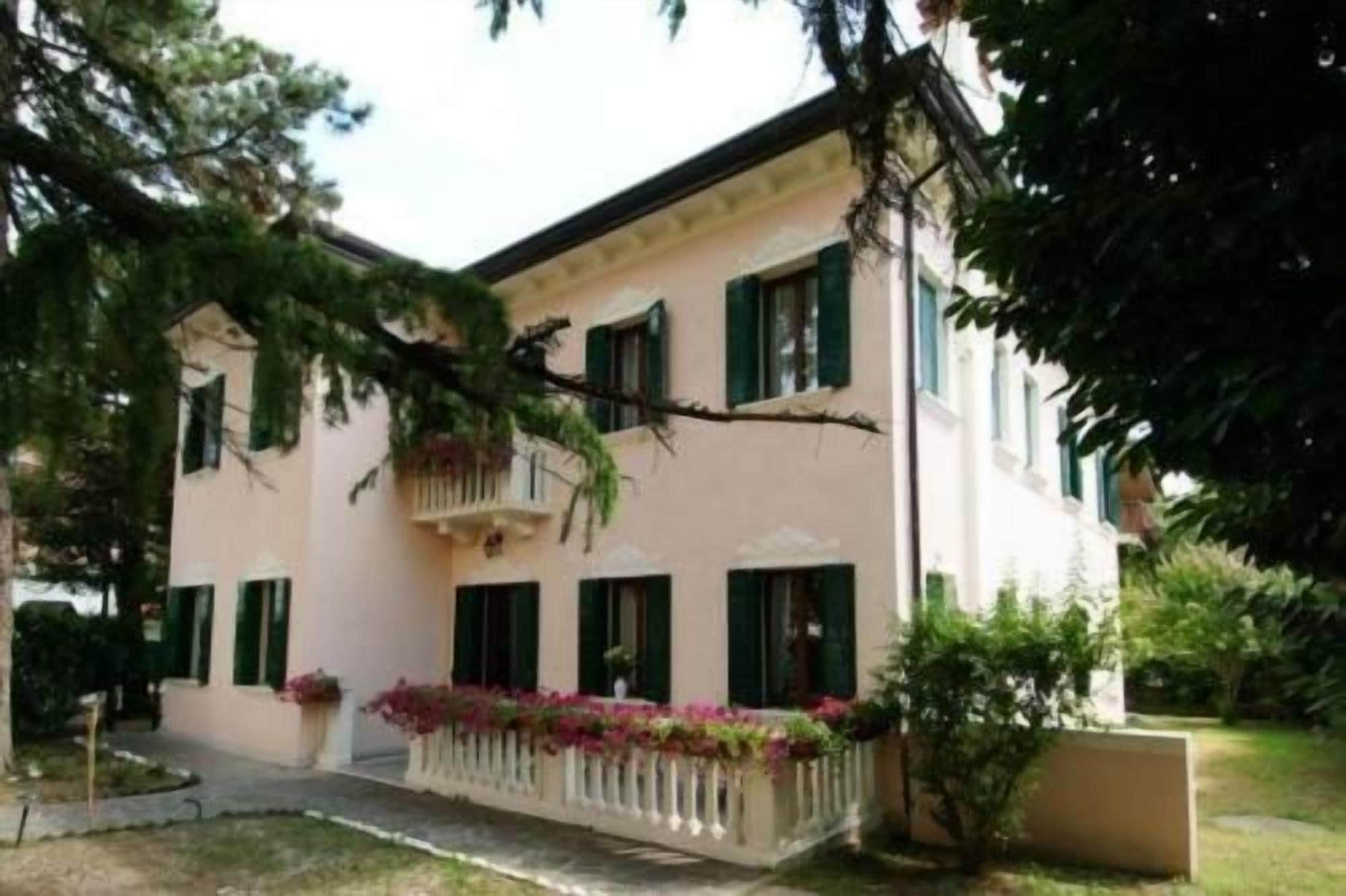 A two-story building with a balcony, a garden with flowers, and a pathway leading to the entrance.