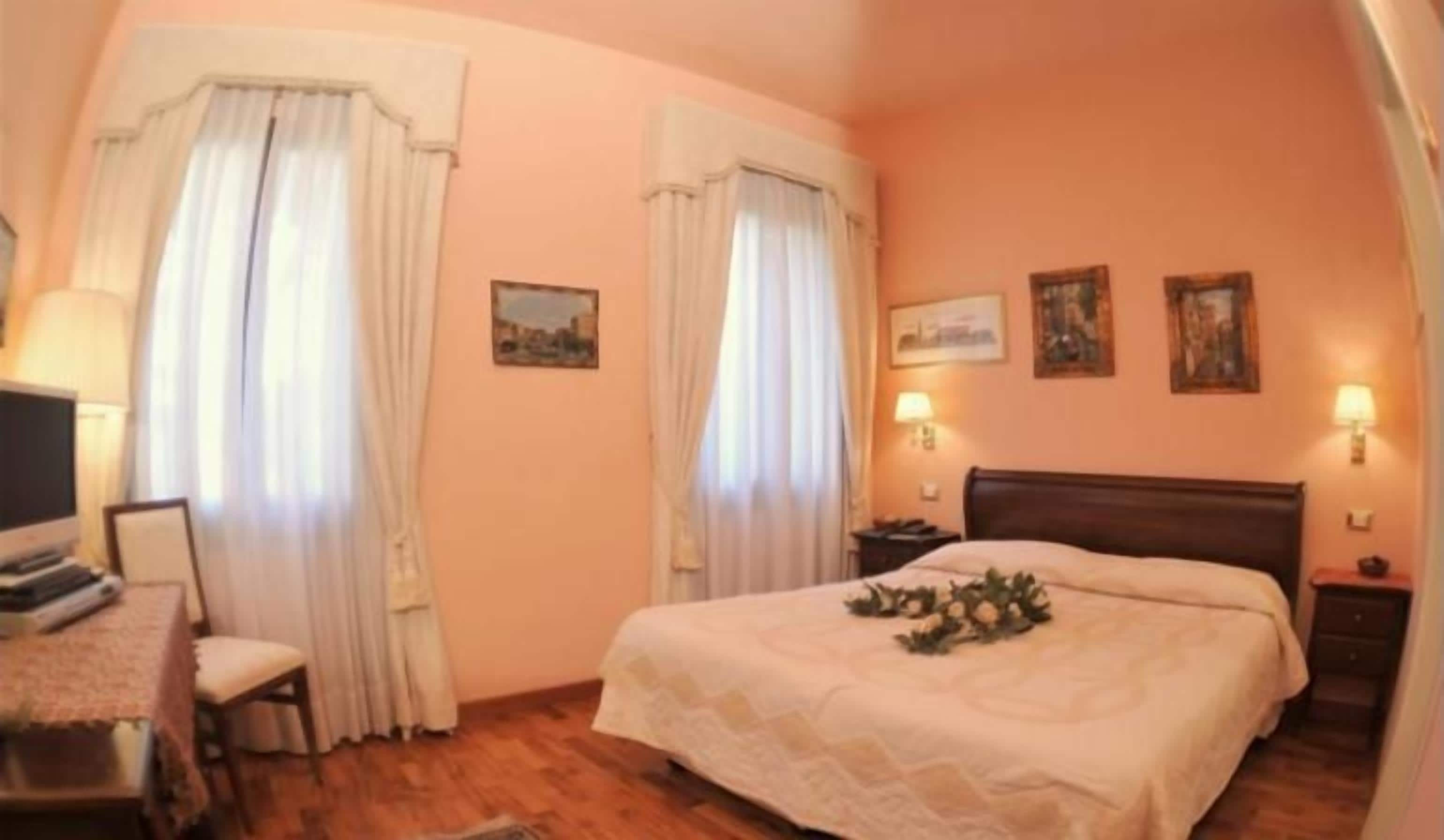 Een slaapkamer met een bed, nachtkastjes, een bureau met stoel, en gordijnen.