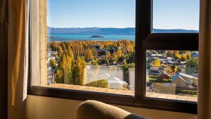 Una habitación con un ventanal que ofrece vistas a un lago, árboles y montañas distantes.