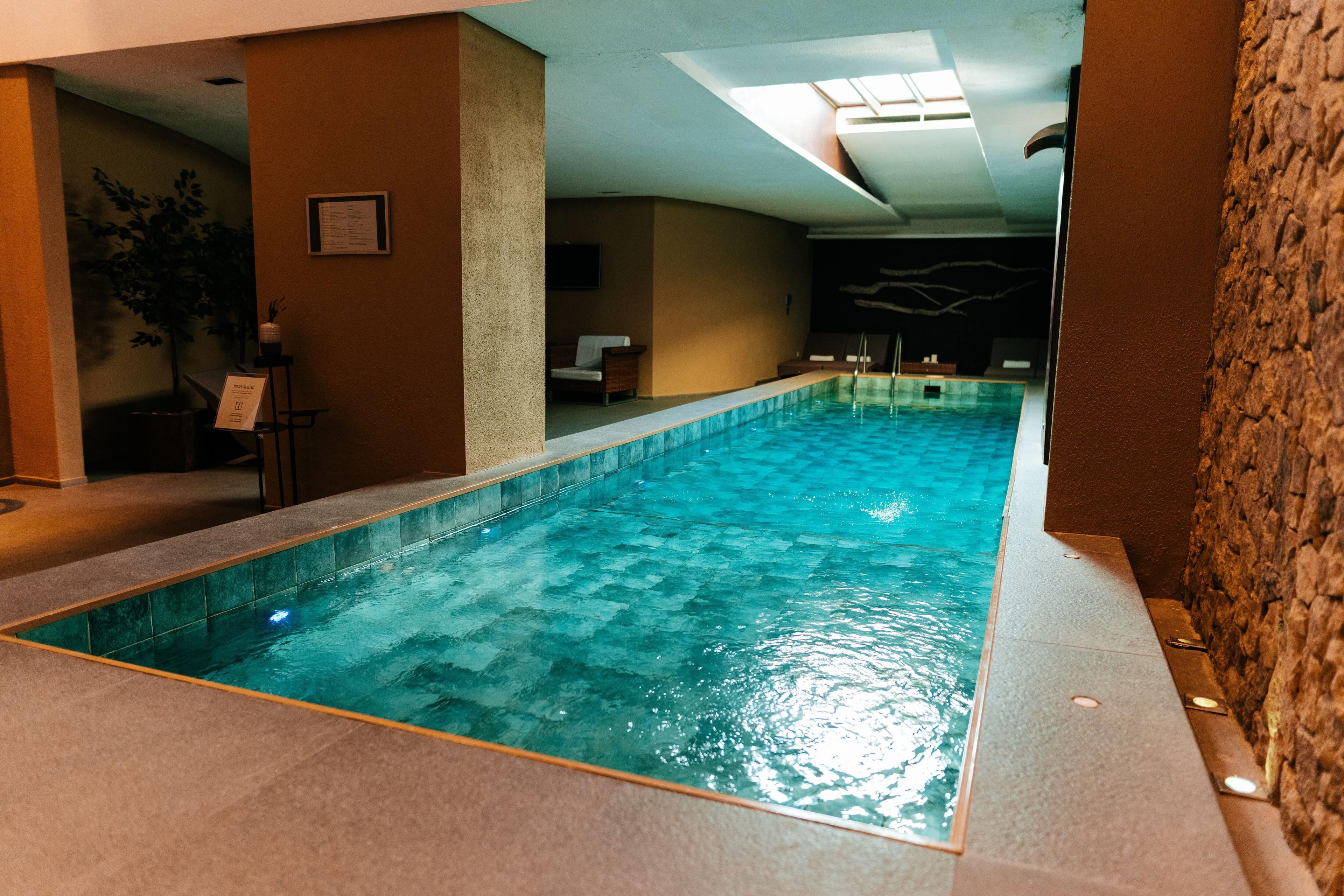An indoor swimming pool with clear water, surrounded by walls and a ceiling with skylights.