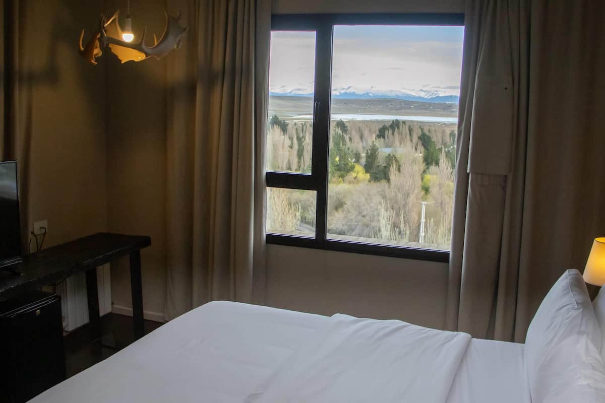 Une chambre d’hôtel équipée d’un lit, d’un bureau, d’une télévision et d’une fenêtre donnant sur un paysage montagneux.