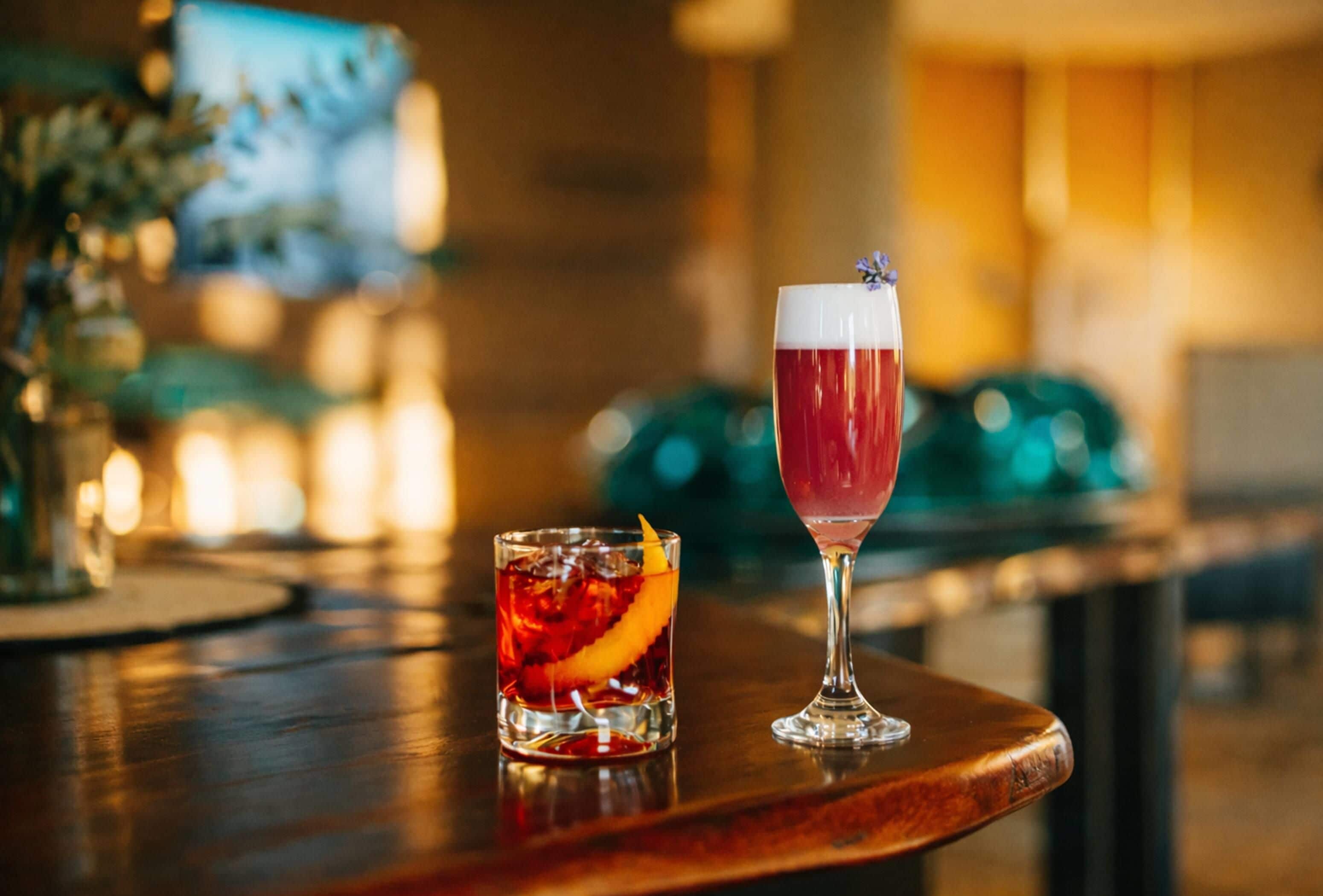 Two glasses of red beverage on a wooden bar counter.
