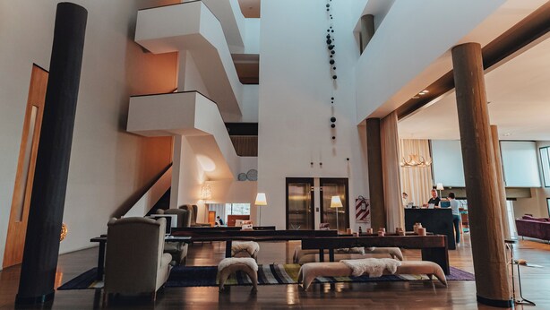 Un vestíbulo espacioso con diseño moderno, que incluye una zona de estar central, un mostrador de recepción y una escalera que conduce a plantas superiores.