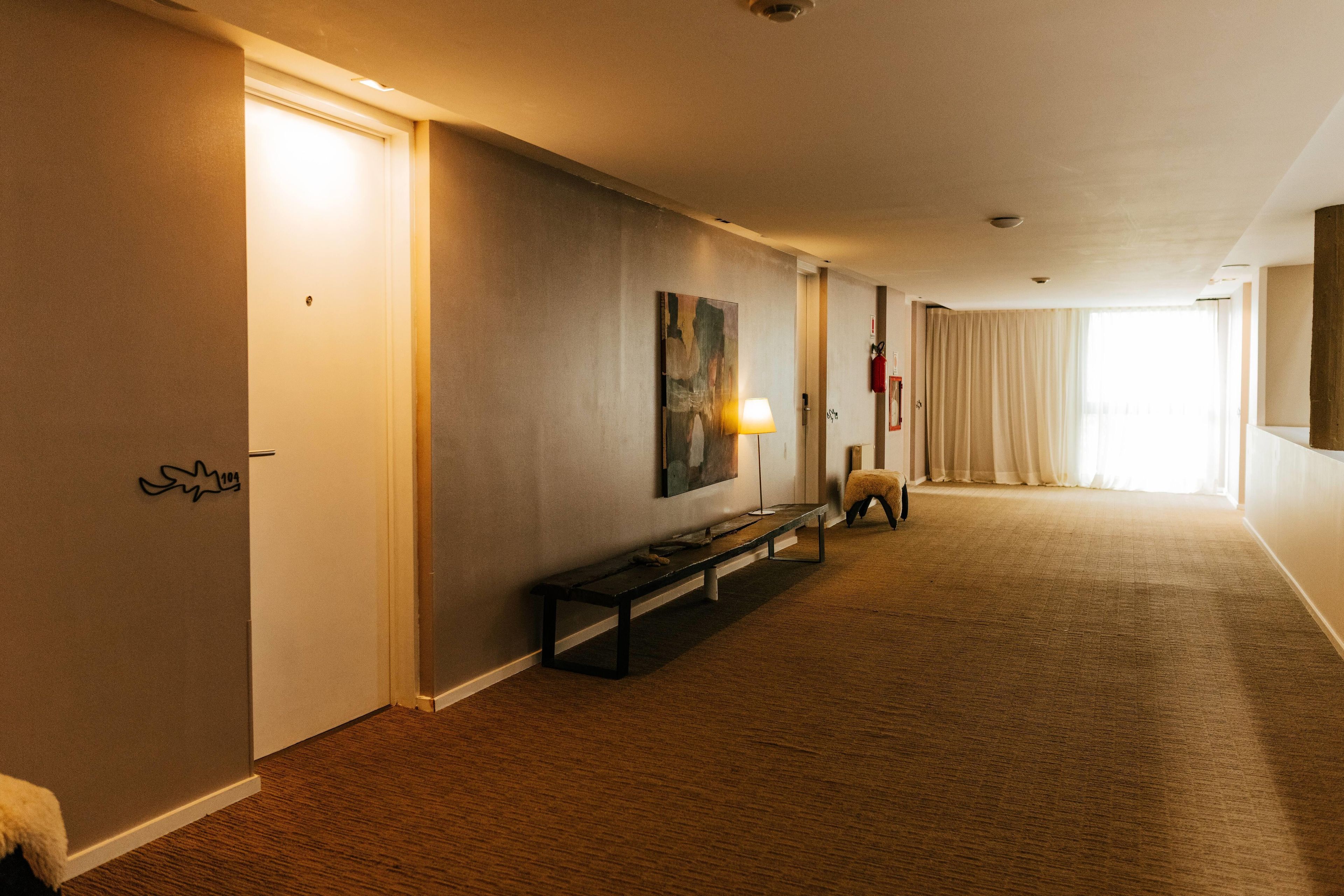 A hotel hallway with a bench, a painting, and a fire extinguisher.