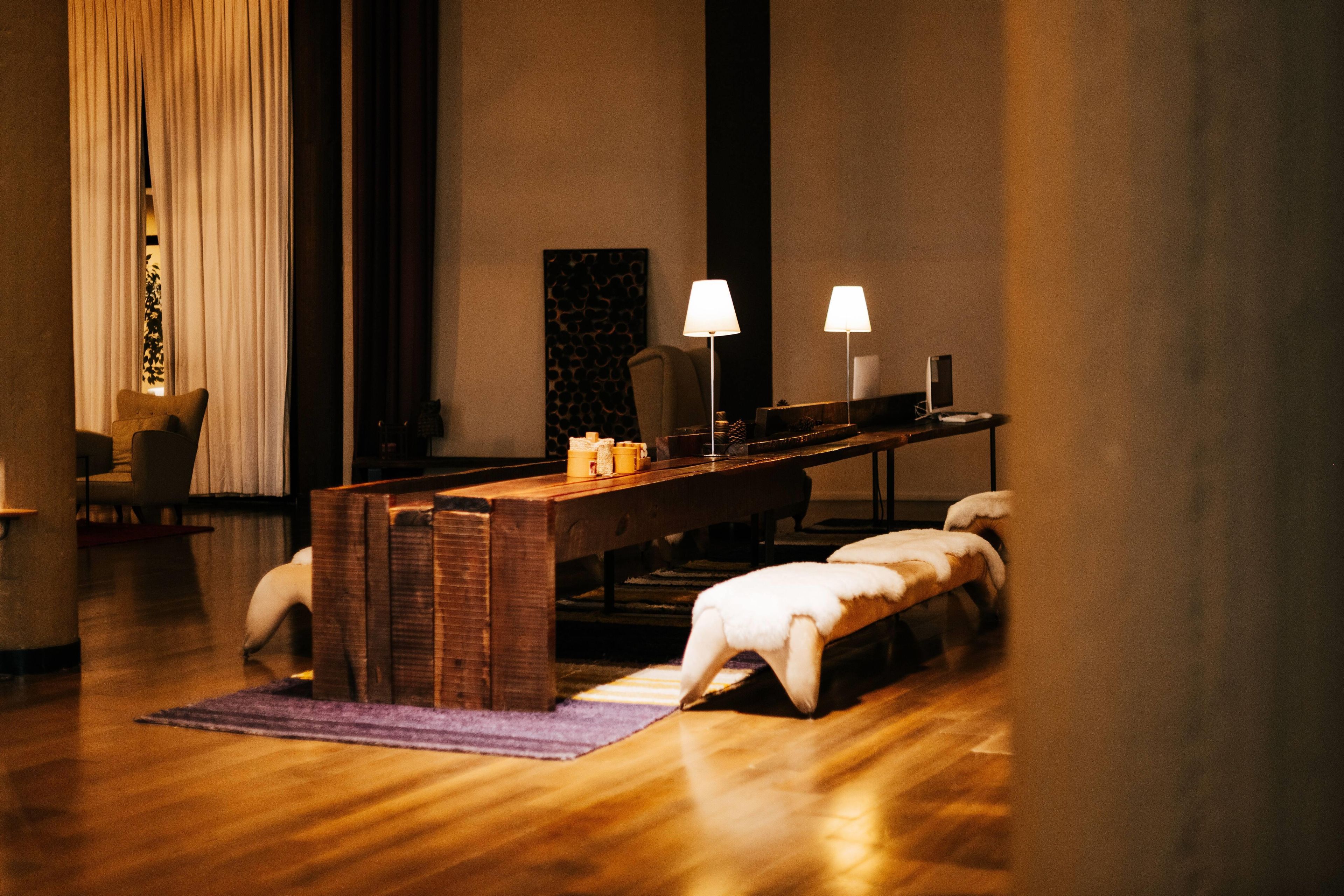Una habitación moderna con un banco de madera, dos lámparas, una mesa con objetos y una silla.