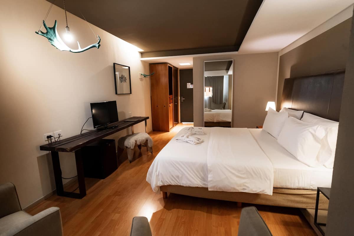 Une chambre d’hôtel moderne dotée d’un bureau en bois, d’un téléviseur à écran plat, d’un lit avec du linge de maison blanc et d’un luminaire au plafond au design original.