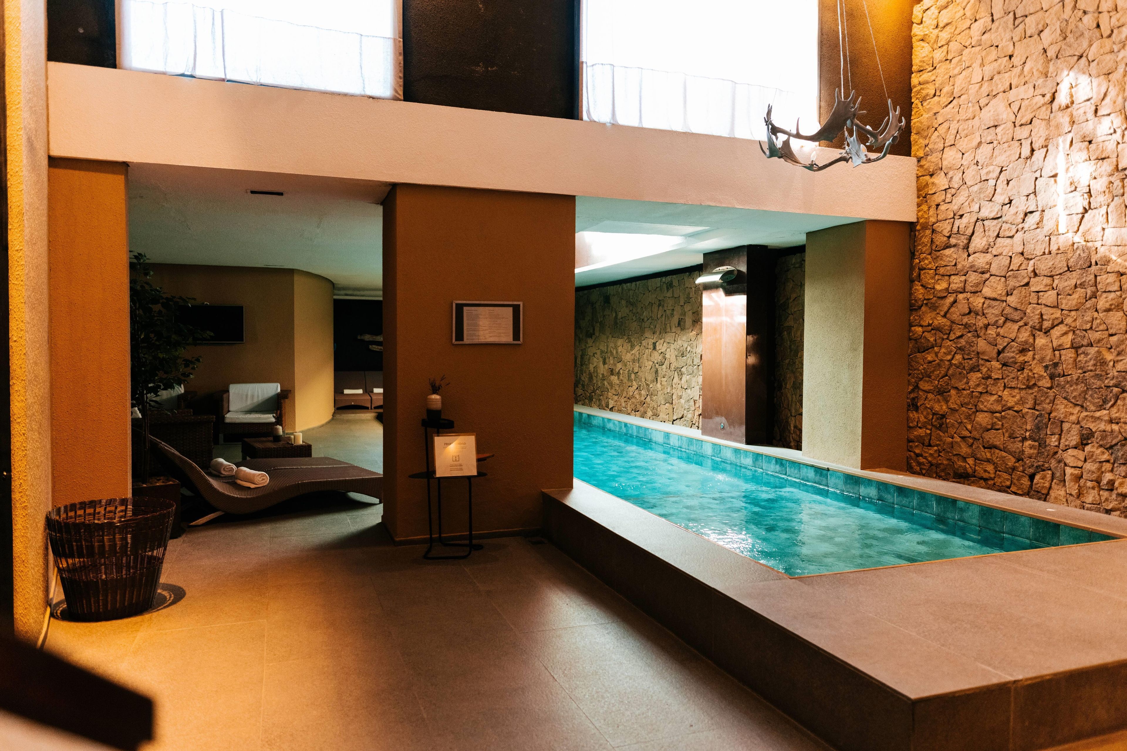 Un espacio de spa con piscina, sillas de descanso y una pared de piedra.
