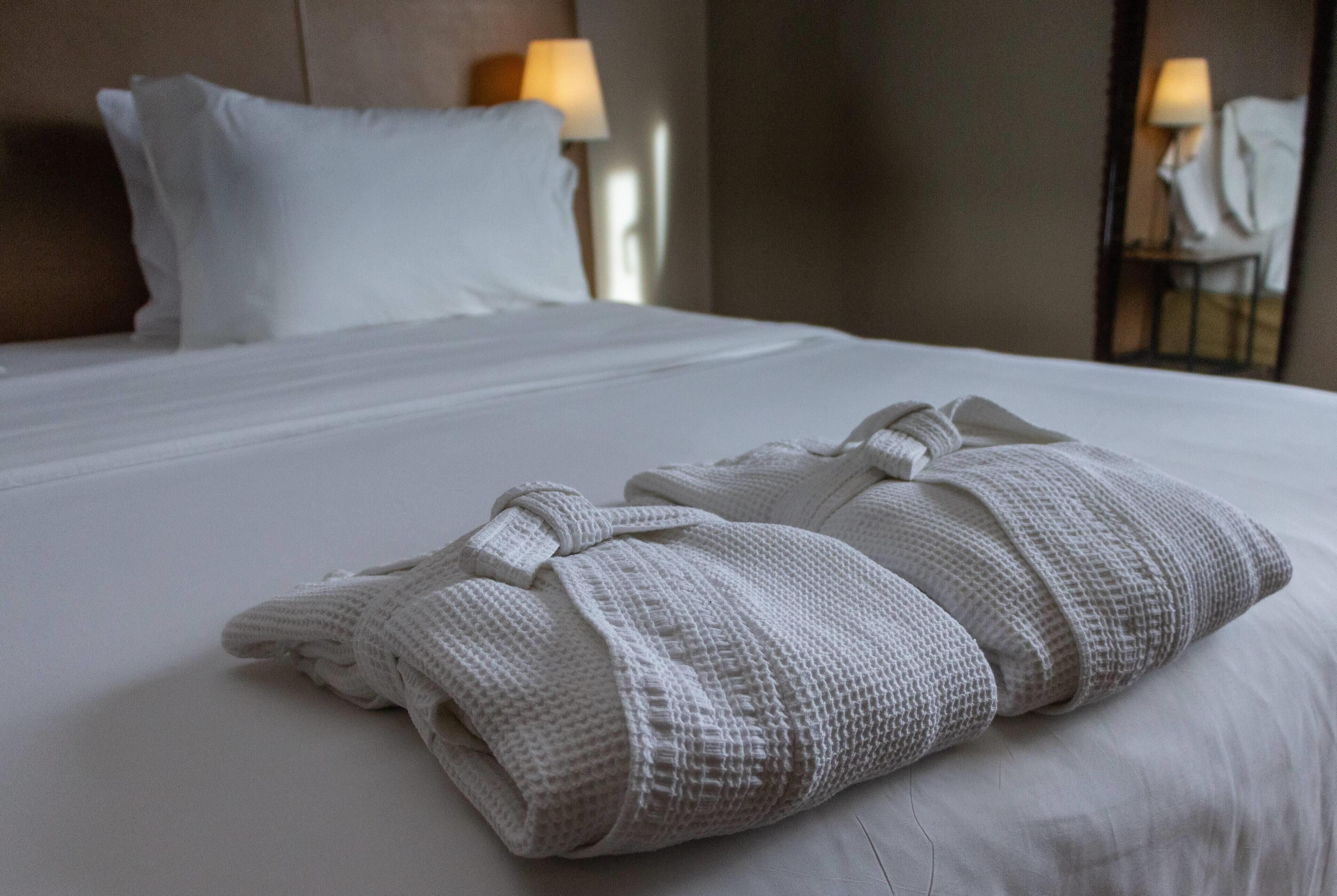 Un lit bien fait, avec du linge de lit blanc et deux serviettes pliées posées sur le lit.