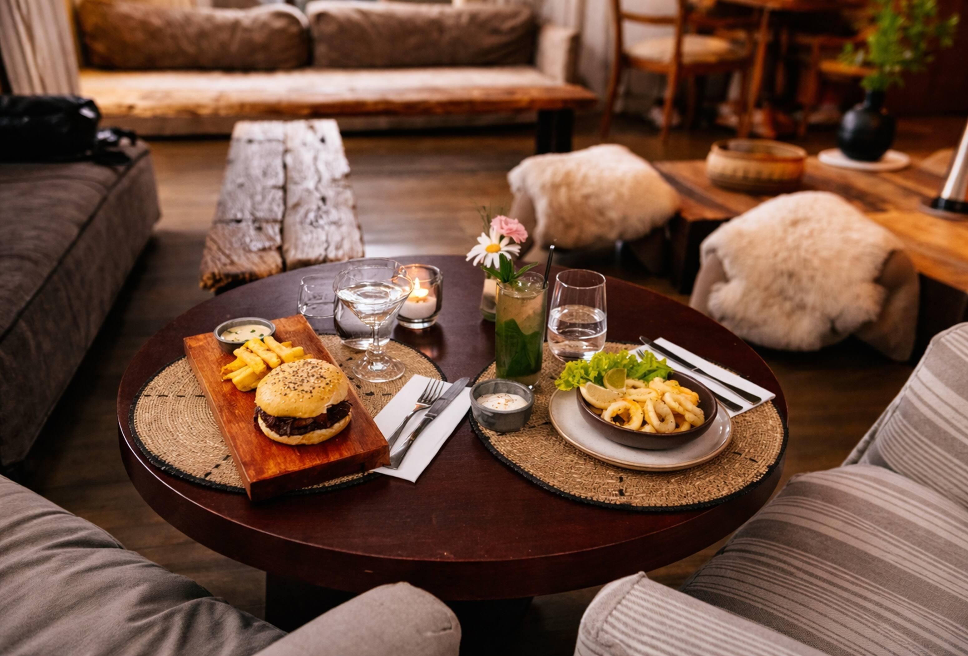 Mesa de madeira redonda com um hambúrguer, batatas fritas, uma salada e bebidas.