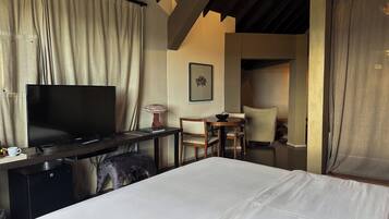 A hotel room with a bed, a desk with a TV, a chair, a small table, and a lamp.