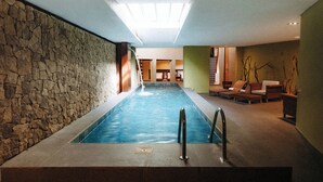 Una piscina con un muro de piedra en un lado y una zona de descanso con sillones en el otro.