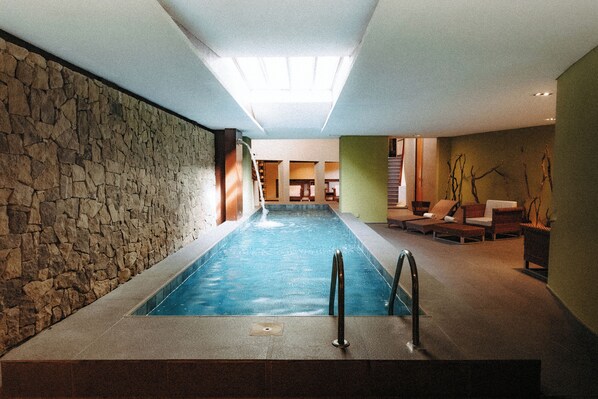 Una piscina con un muro de piedra en un lado y una zona de descanso con sillones en el otro.