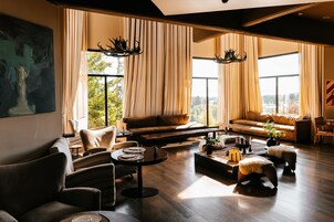 A spacious living room with a large window, a sofa set, a coffee table, and a painting on the wall.