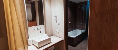 A modern bathroom with a large mirror, a white sink, and a bathtub.