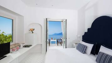 Una habitación de hotel moderna con una cama grande, un televisor, un balcón con vistas al mar y una pequeña mesa con sillas.
