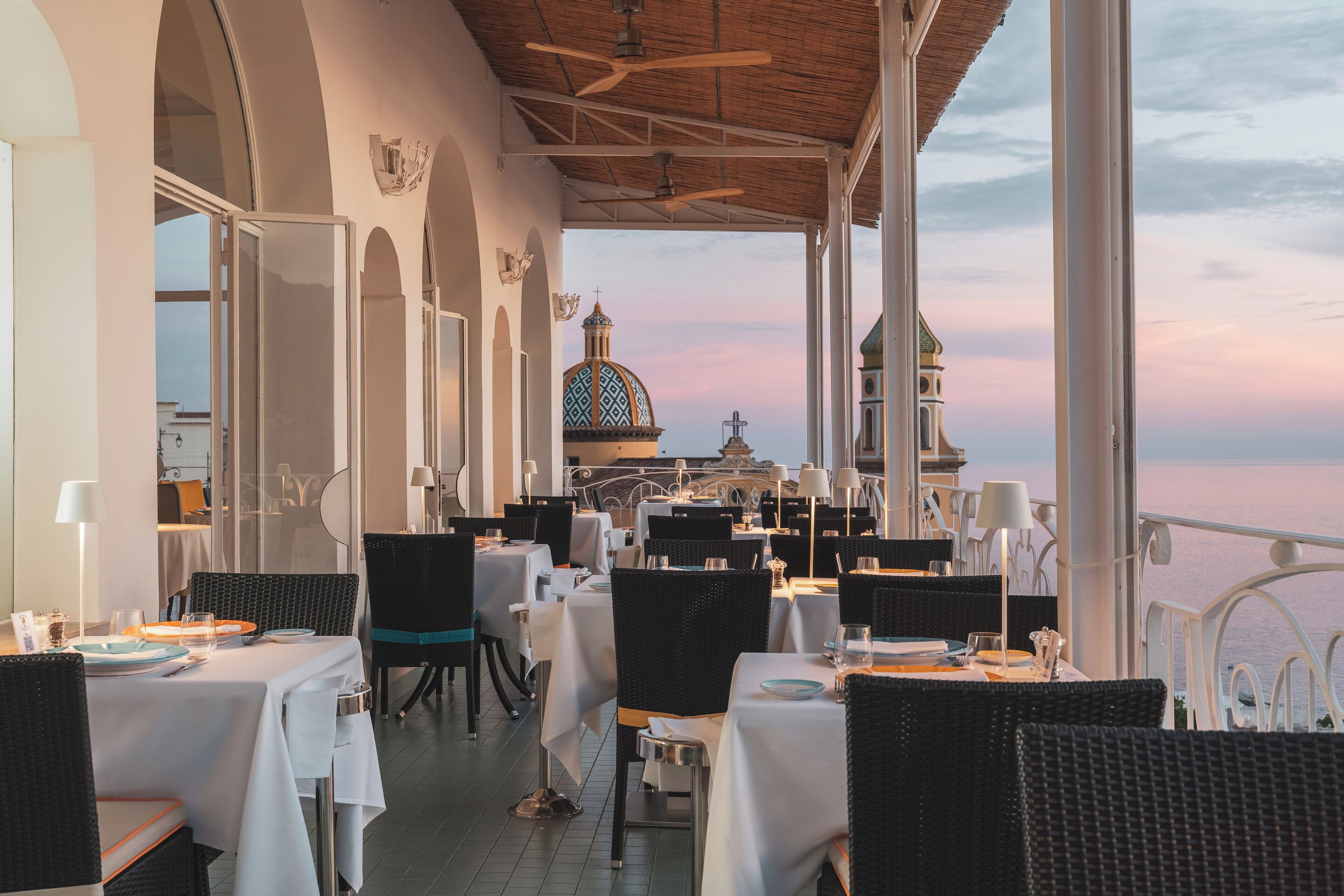 A restaurant with tables set for dining, a view of a domed building, and a balcony with a railing.