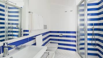 Un baño moderno con un lavamanos blanco, una cabina de ducha con mampara de vidrio y azulejos a rayas azules.