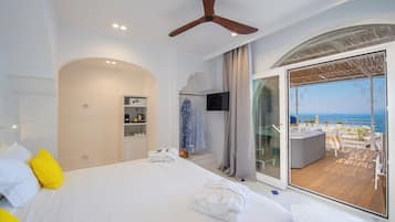 Habitación de hotel con cama, ventilador de techo, televisor, minibar y balcón con vista al mar.