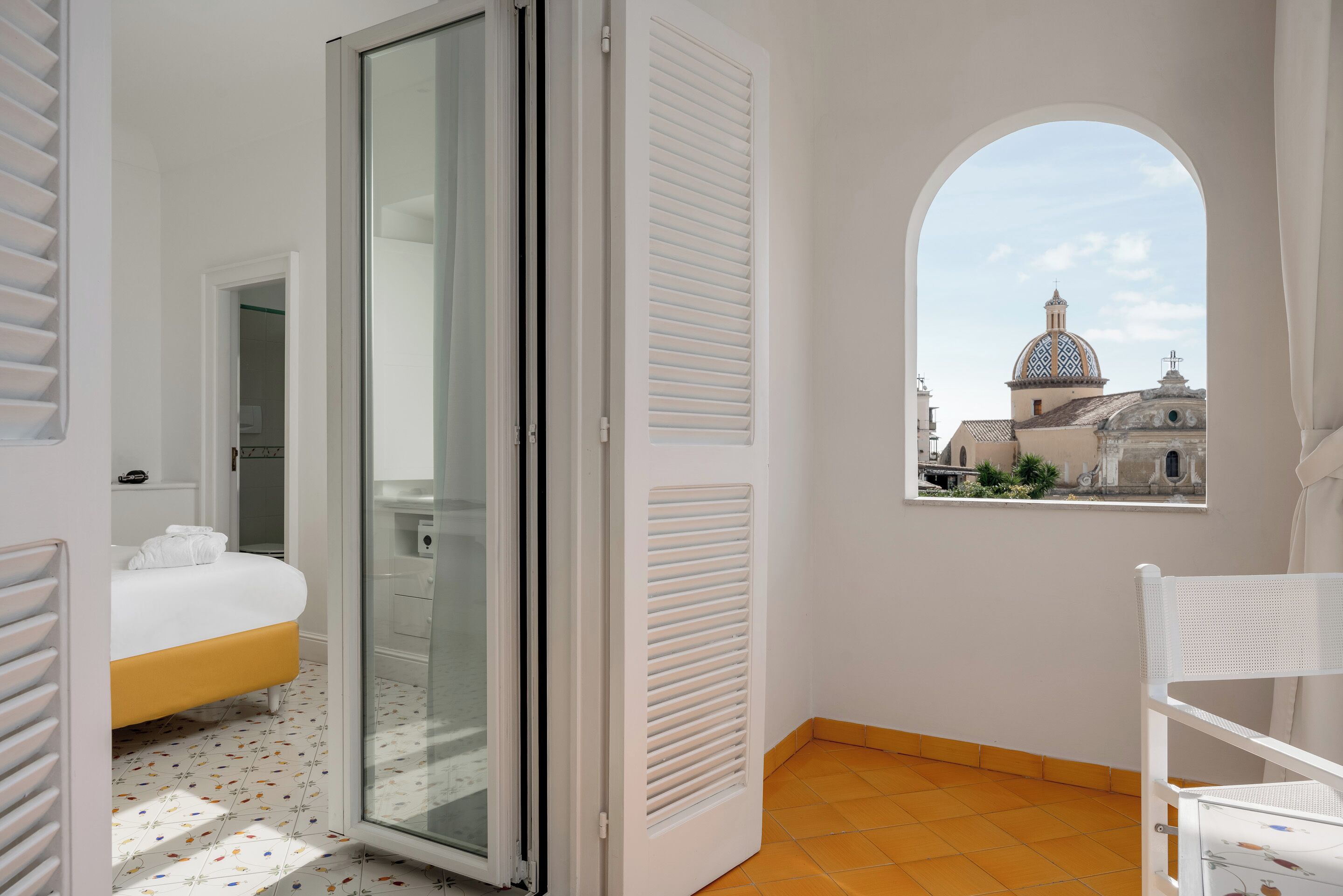 A bedroom with a bed, a sliding glass door, a window with a view of a building, and a white chair.