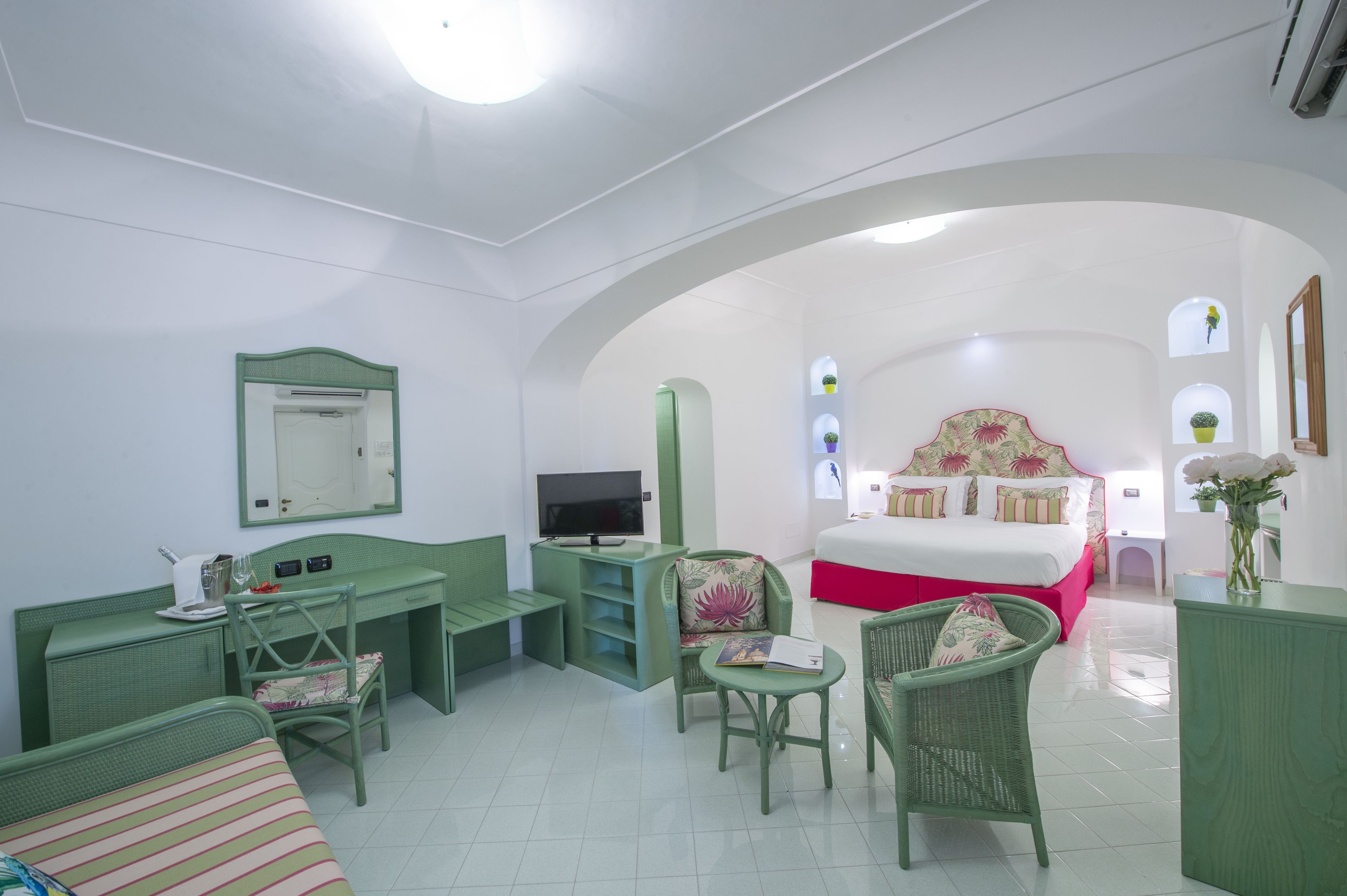A room with a bed, desk, chairs, and a TV.