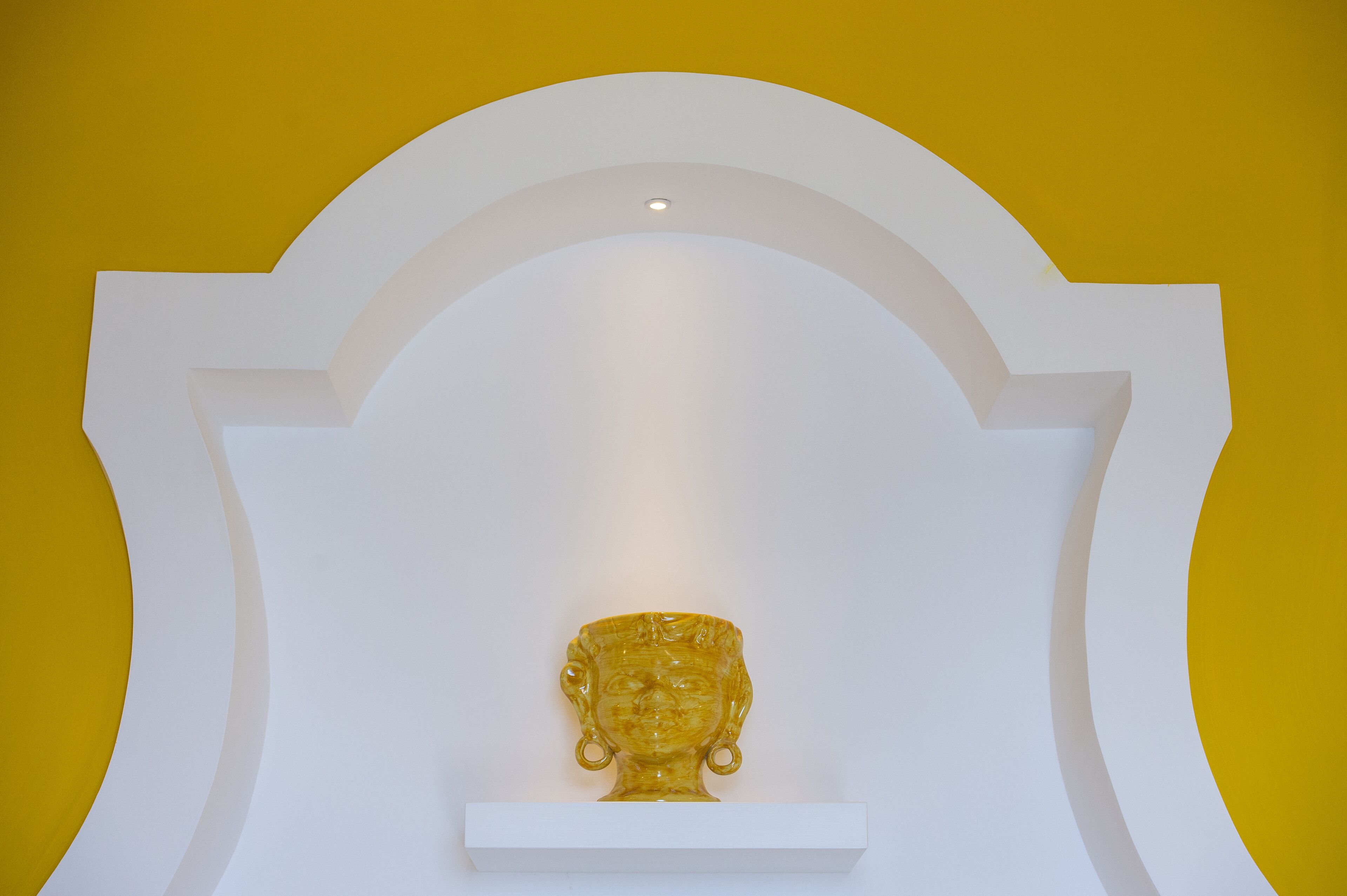 A golden sculpture on a white pedestal against a yellow wall.