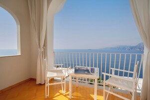 Un balcón con sillas y una mesa blancos, con vista al mar.