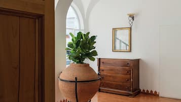 Una habitación con puerta de madera, una planta grande en maceta, un aparador de madera y un espejo fijado a la pared.