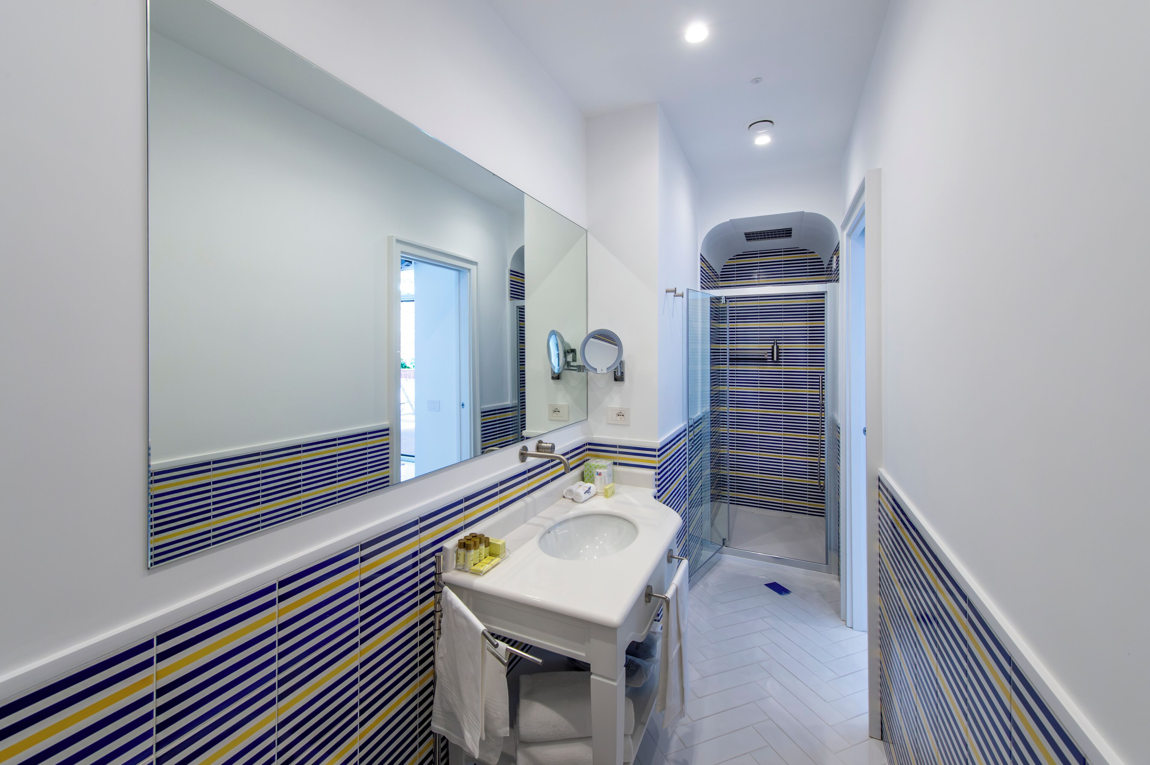 Un baño moderno con un espejo grande, un lavabo y azulejos rayados en la pared.