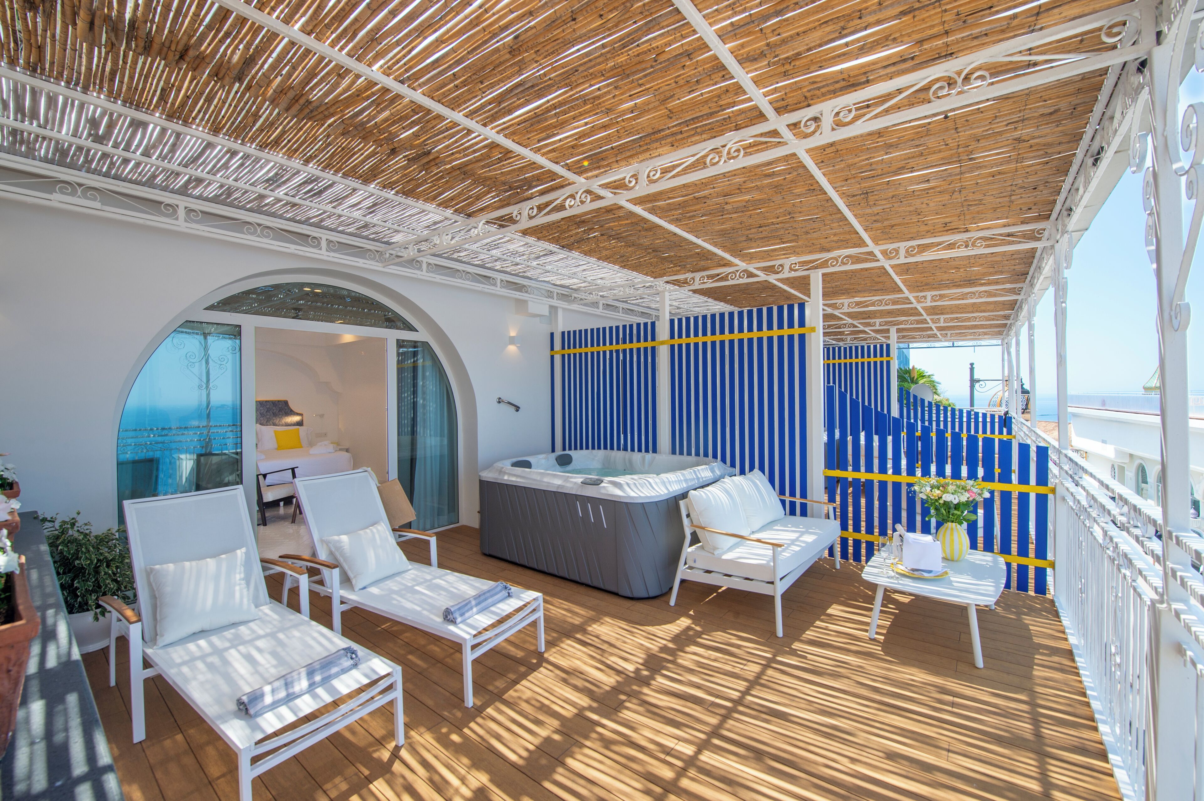 A sunlit outdoor deck with lounge chairs, a hot tub, and a view of the sea.