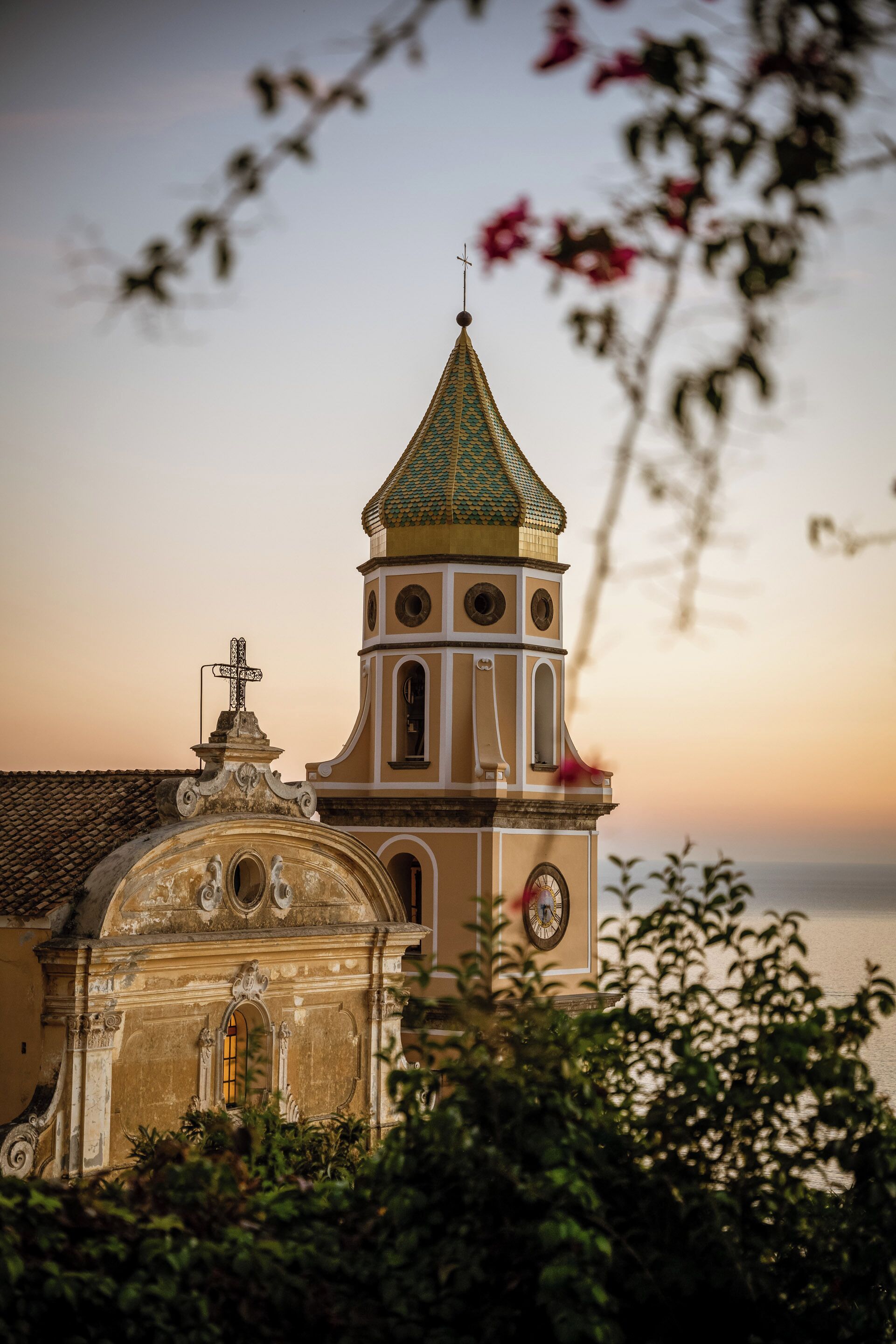A church with a green dome and a cross on top, surrounded by greenery.