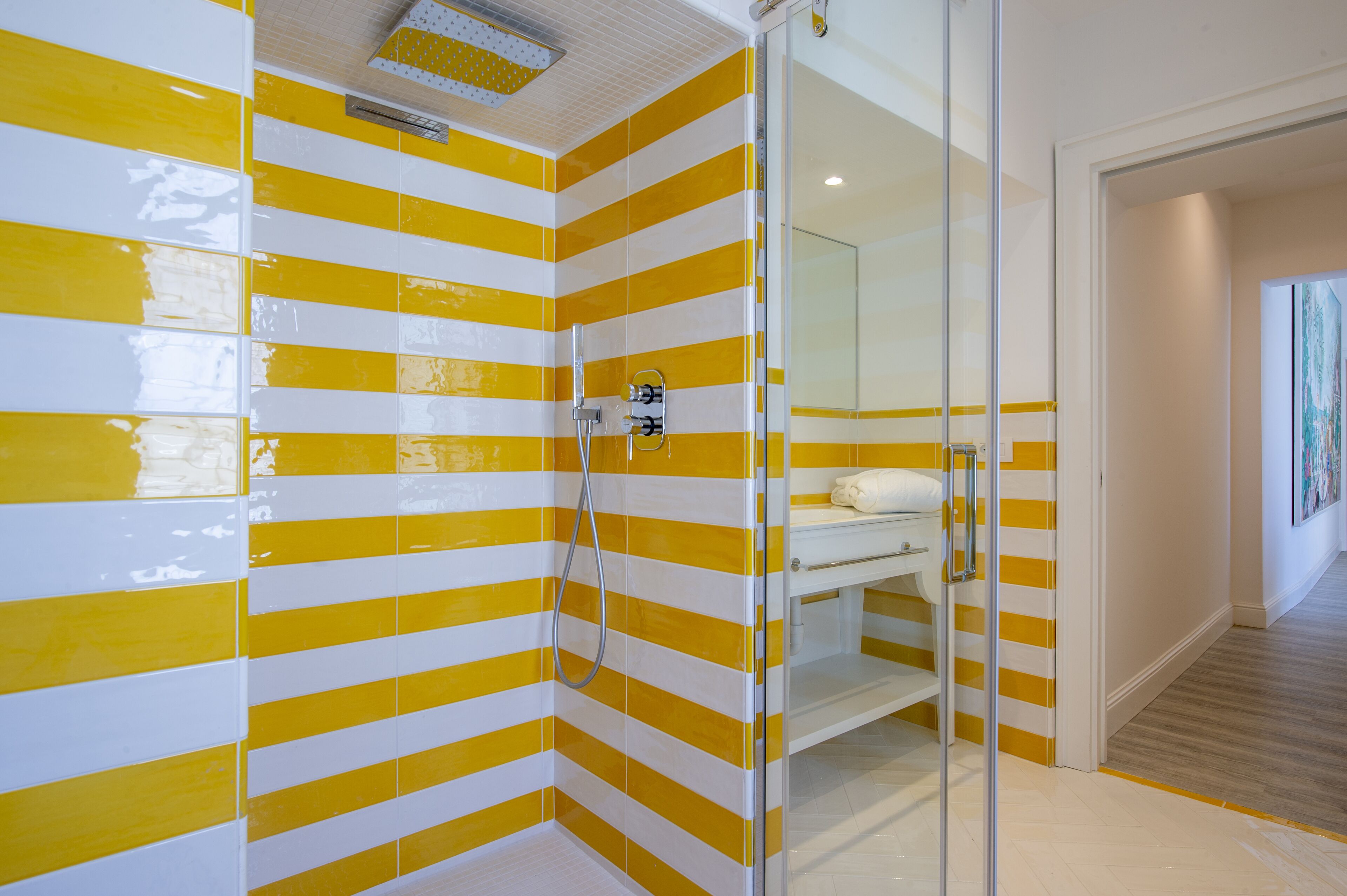 A bathroom with yellow and white striped walls, a glass shower enclosure, and a white sink with a towel.