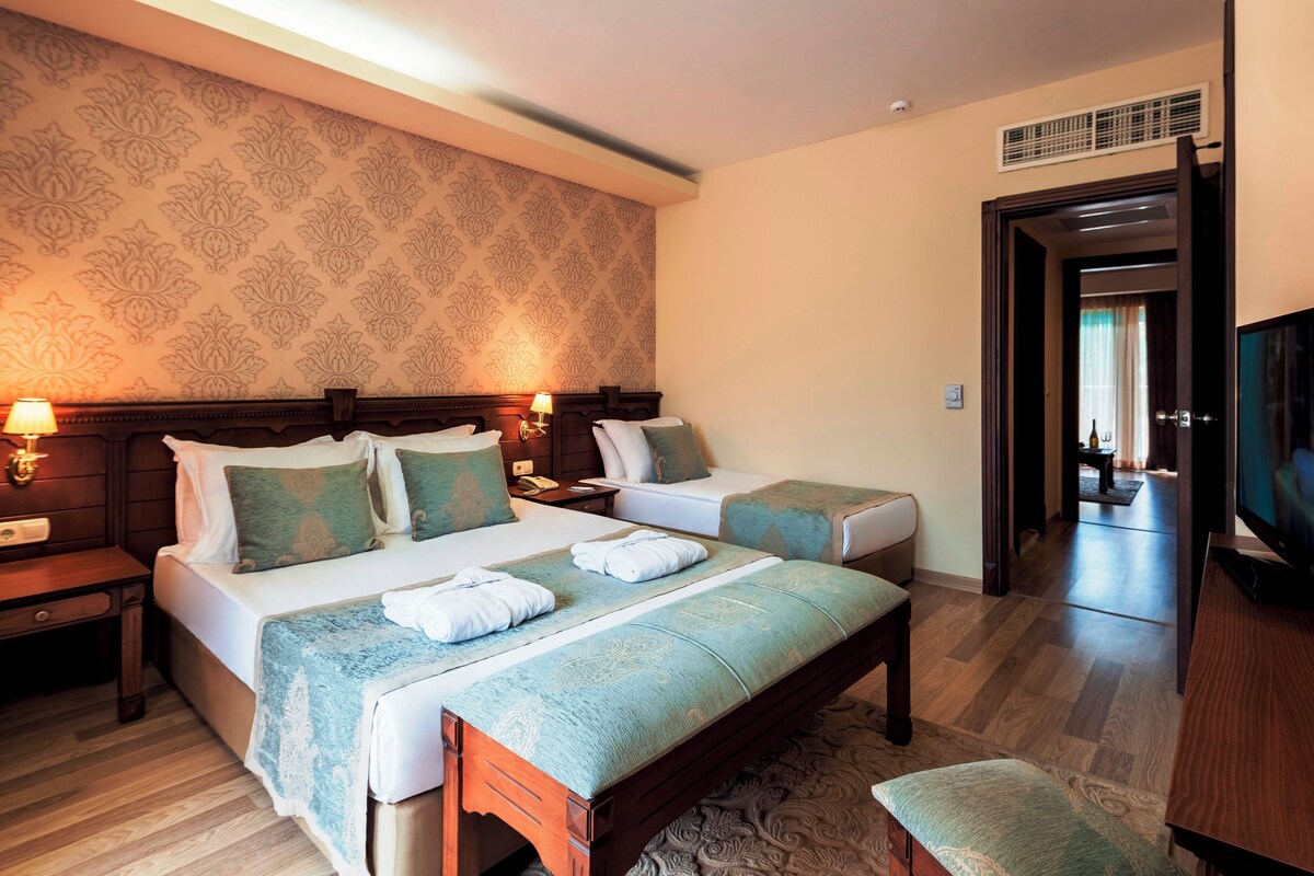 Habitació d'hotel amb dos llits, un escriptori, televisió i bany visible a través d'una porta oberta.