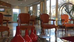 Eine Lobby mit mehreren Holzsesseln, einem Empfangsbereich und großen Fenstern.