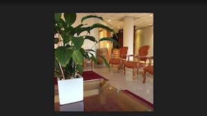 Eine Lobby mit einer großen Topfpflanze, Holzstühlen und einem gefliesten Boden.