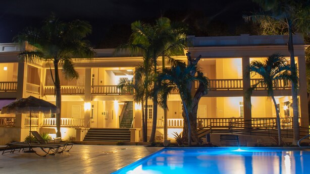 A hotel with a pool, palm trees, and a well-lit balcony area.