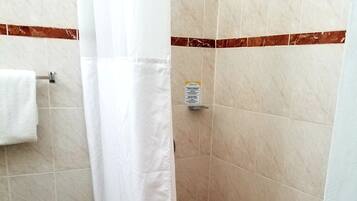 Pequeño espacio de ducha con azulejos, cortina blanca, una toalla colgada en un perchero y un letrero en la pared.