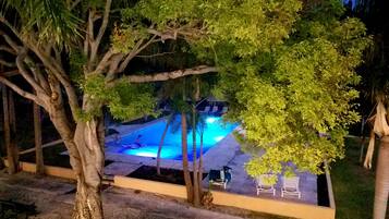 Ein szenischer Blick auf einen Poolbereich bei Nacht, mit klarem Himmel, umgeben von Bäumen und einigen Liegestühlen.