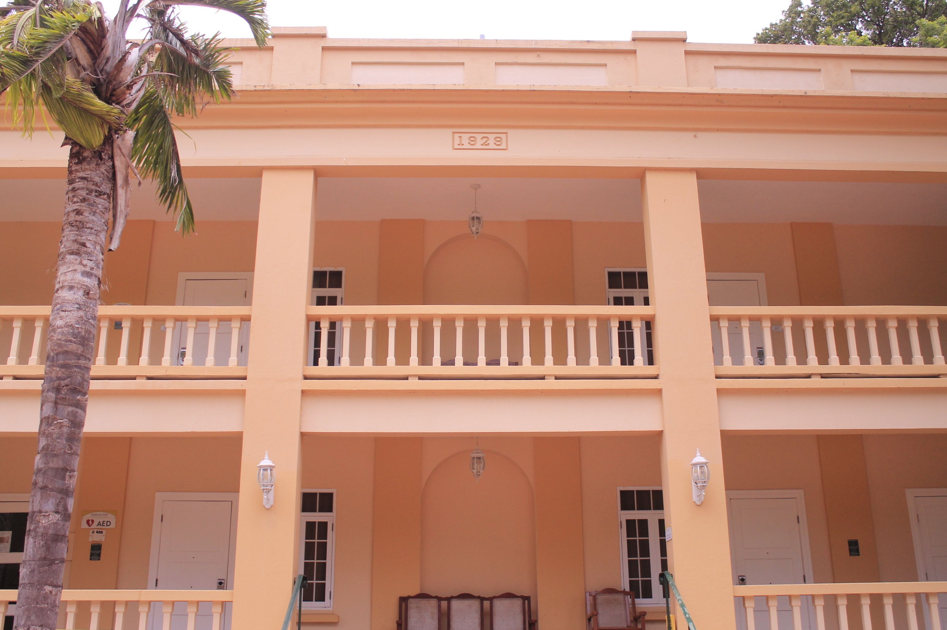 A building with a balcony, a palm tree, and a sign with the year 1929.