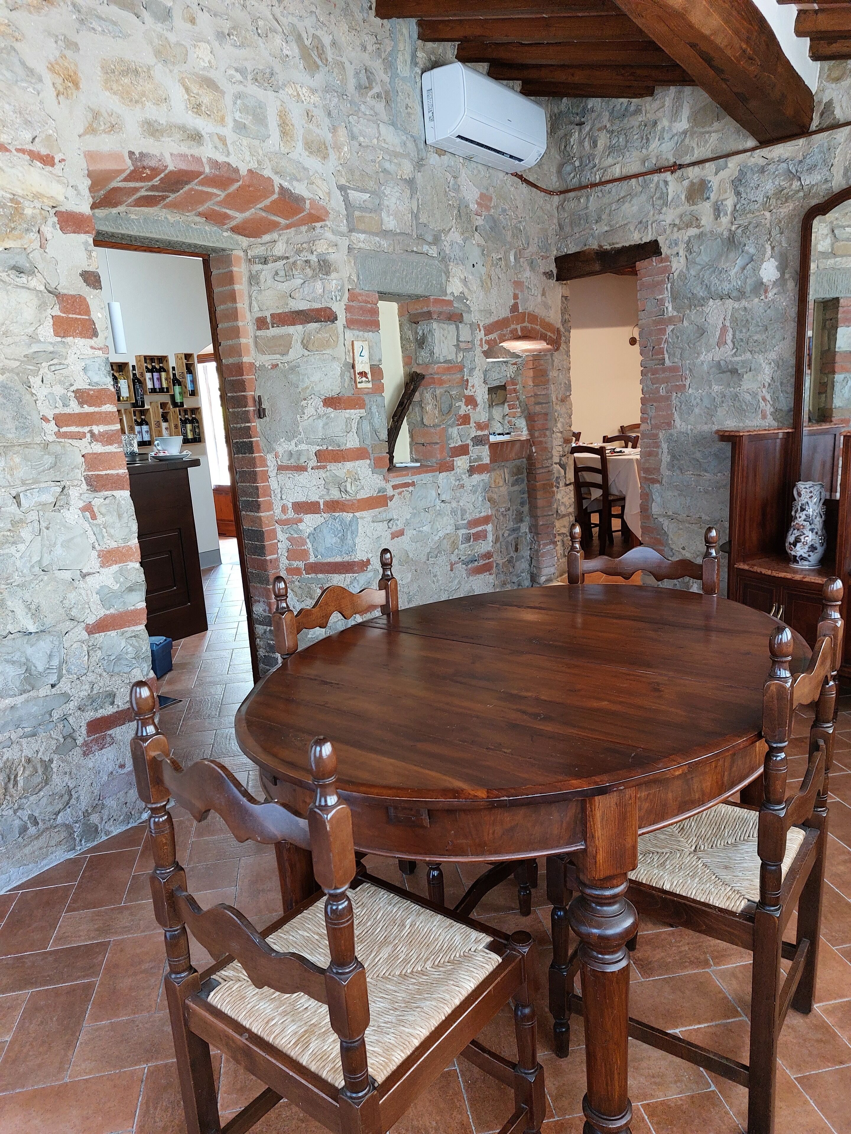 A rustic dining area with a round wooden table and chairs, stone walls, and a brick archway.