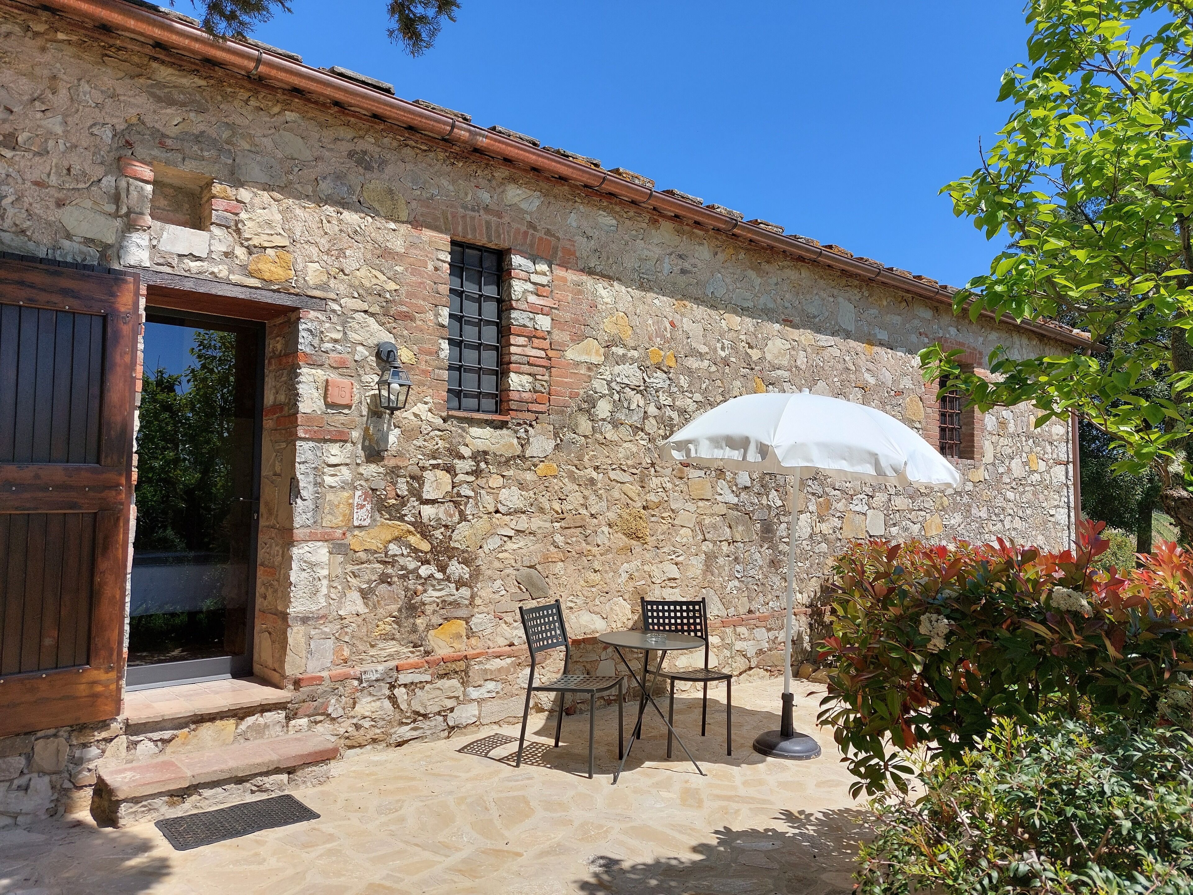 Un bâtiment en pierre avec une porte en bois, une fenêtre et un parasol blanc.