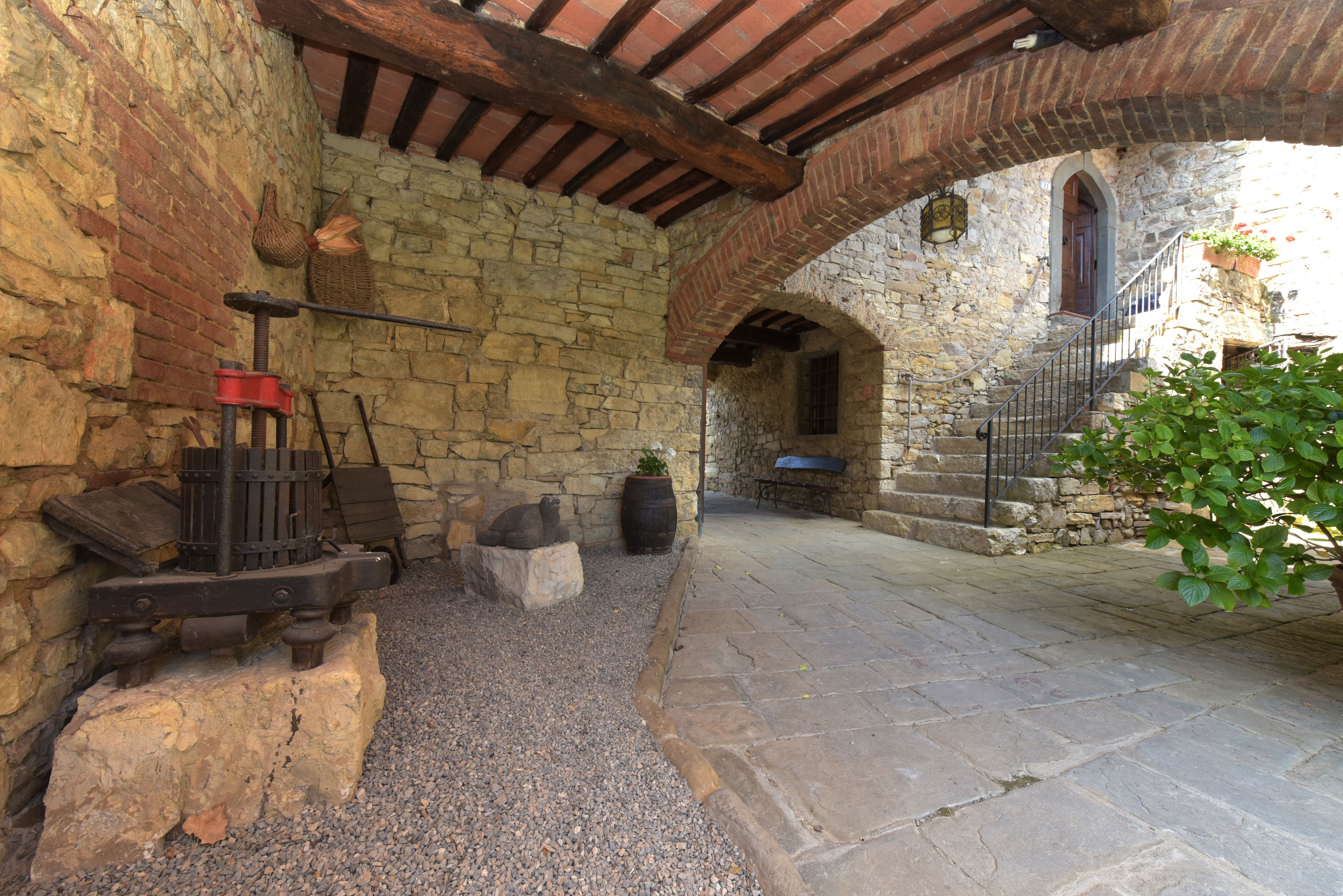 Un cortile in pietra con un rustico muro in pietra, un soffitto con travi in legno e una scala in pietra che conduce a un piano superiore.