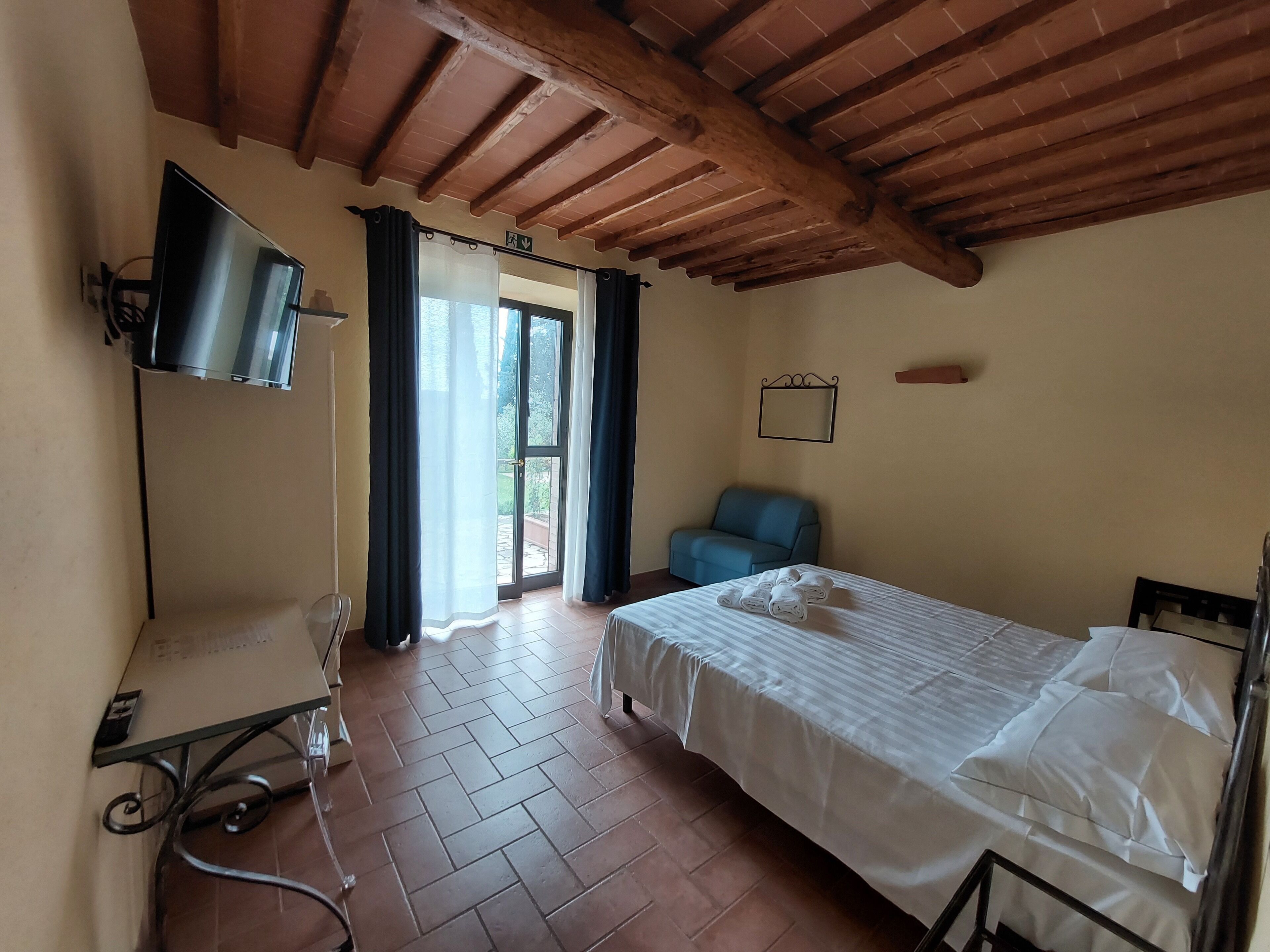 Een hotelkamer met een bed, een bureau met een computer, een stoel en een uitzicht door een deur.