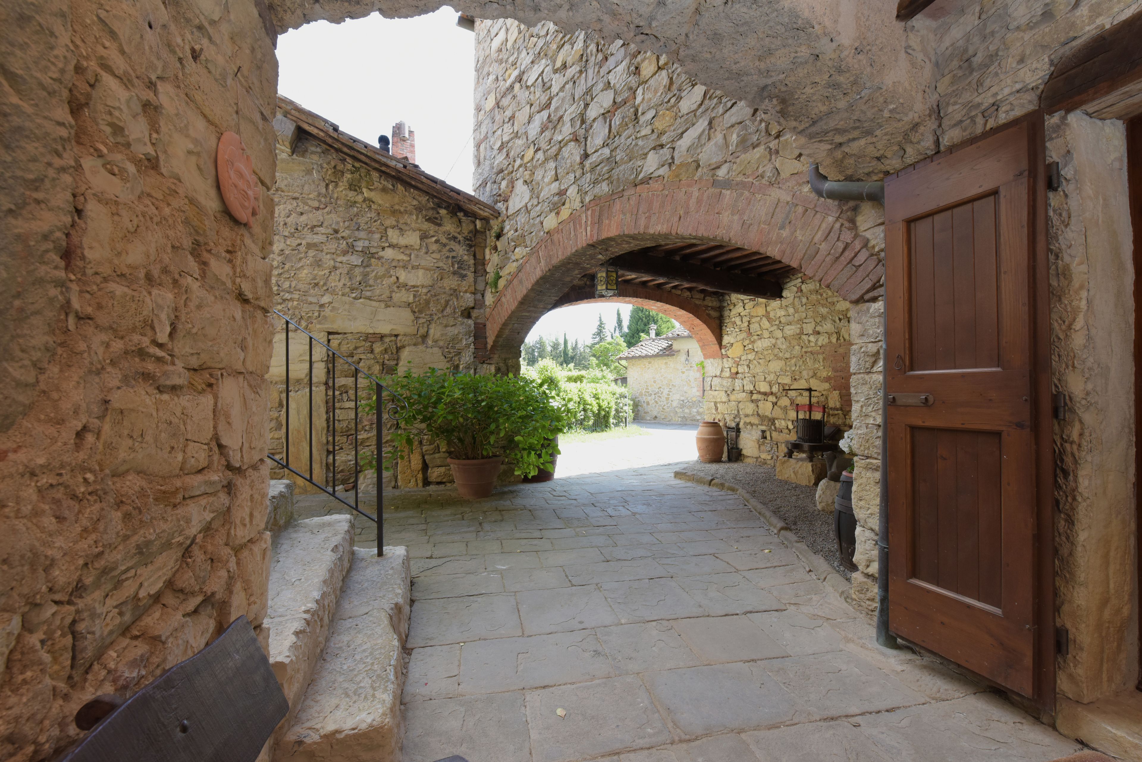 A stone pathway leading to a wooden door, flanked by stone walls and potted plants.