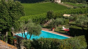 A pool surrounded by lush greenery and vineyards, with a stone building in the background. - Agriturismo San Sano (Gaiole in Chianti)