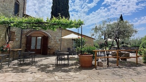 A stone building with a wooden door, outdoor seating, and a pergola with vines. - Agriturismo San Sano (Gaiole in Chianti)