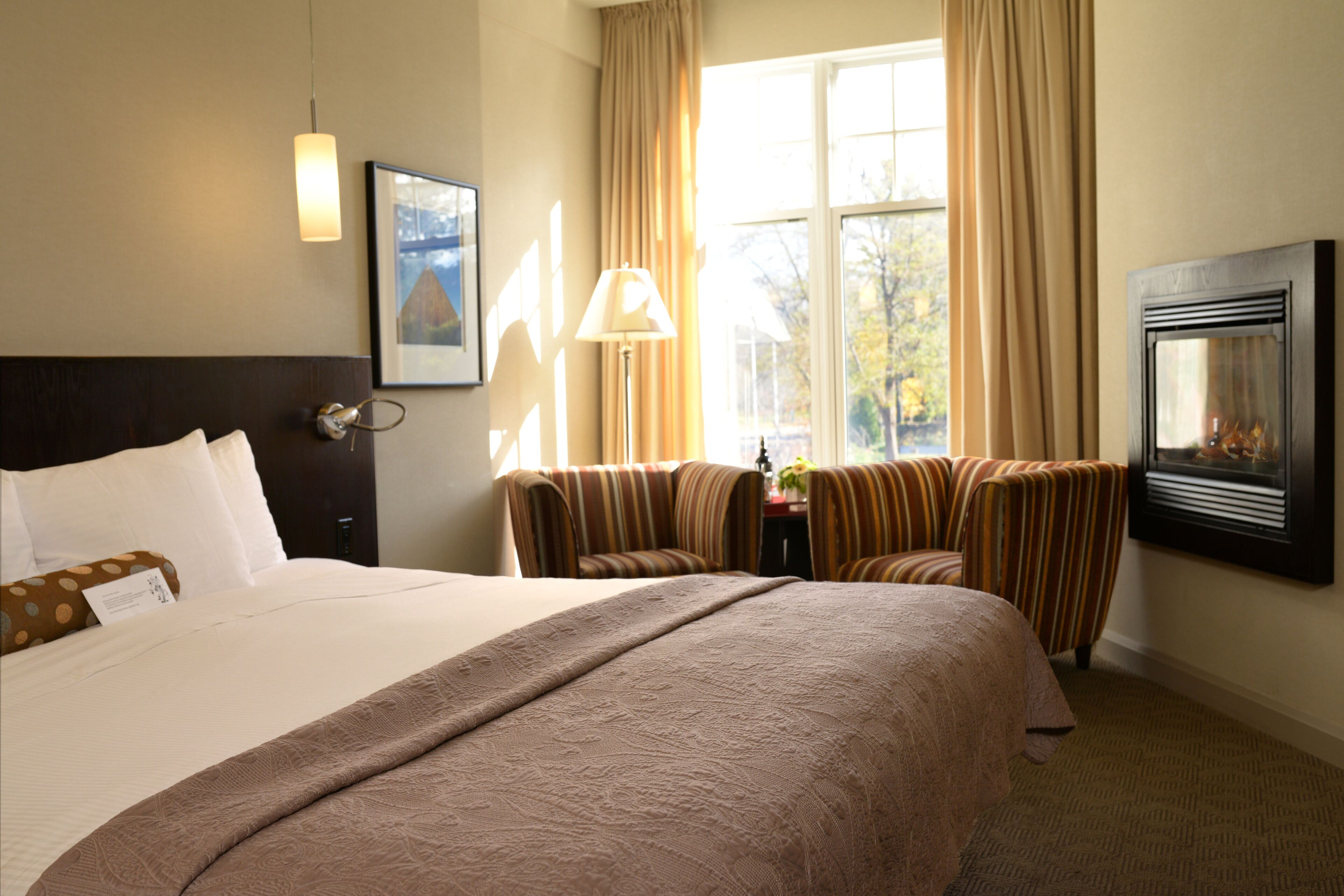 Een hotelkamer met een groot bed, een bureau met lamp, een stoel, een open haard en een raam met gordijnen.