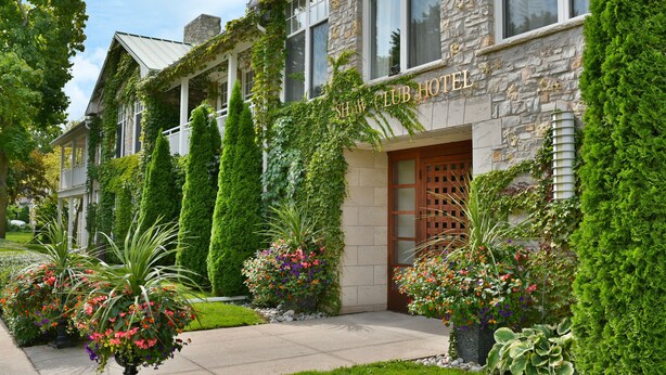 A hotel with a stone facade, a wooden entrance door, and lush greenery. - The Shaw Club Hotel (Niagara-on-the-Lake)