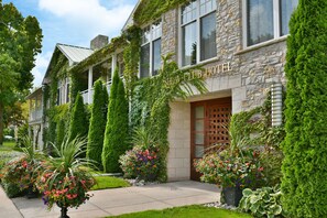Un hôtel à la façade en pierre, doté d’une porte d’entrée en bois et entouré d’une végétation luxuriante.