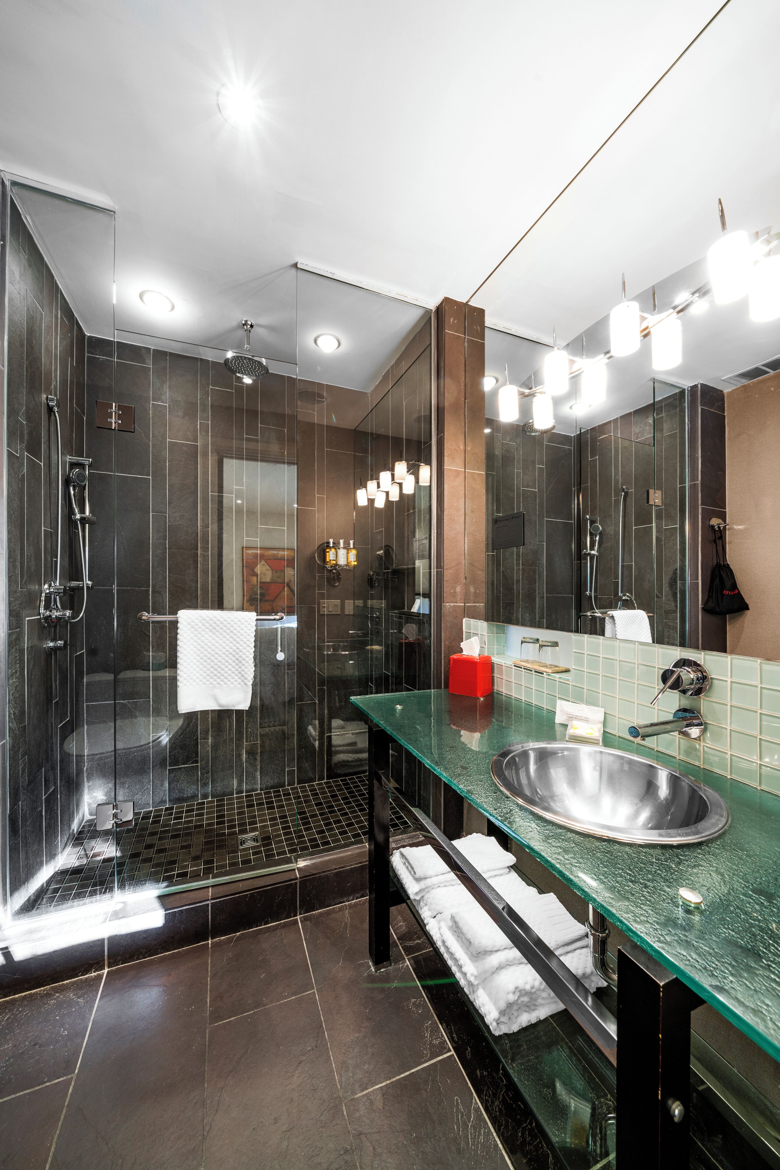A modern bathroom with a glass-enclosed shower, a stainless steel sink, and a large mirror.