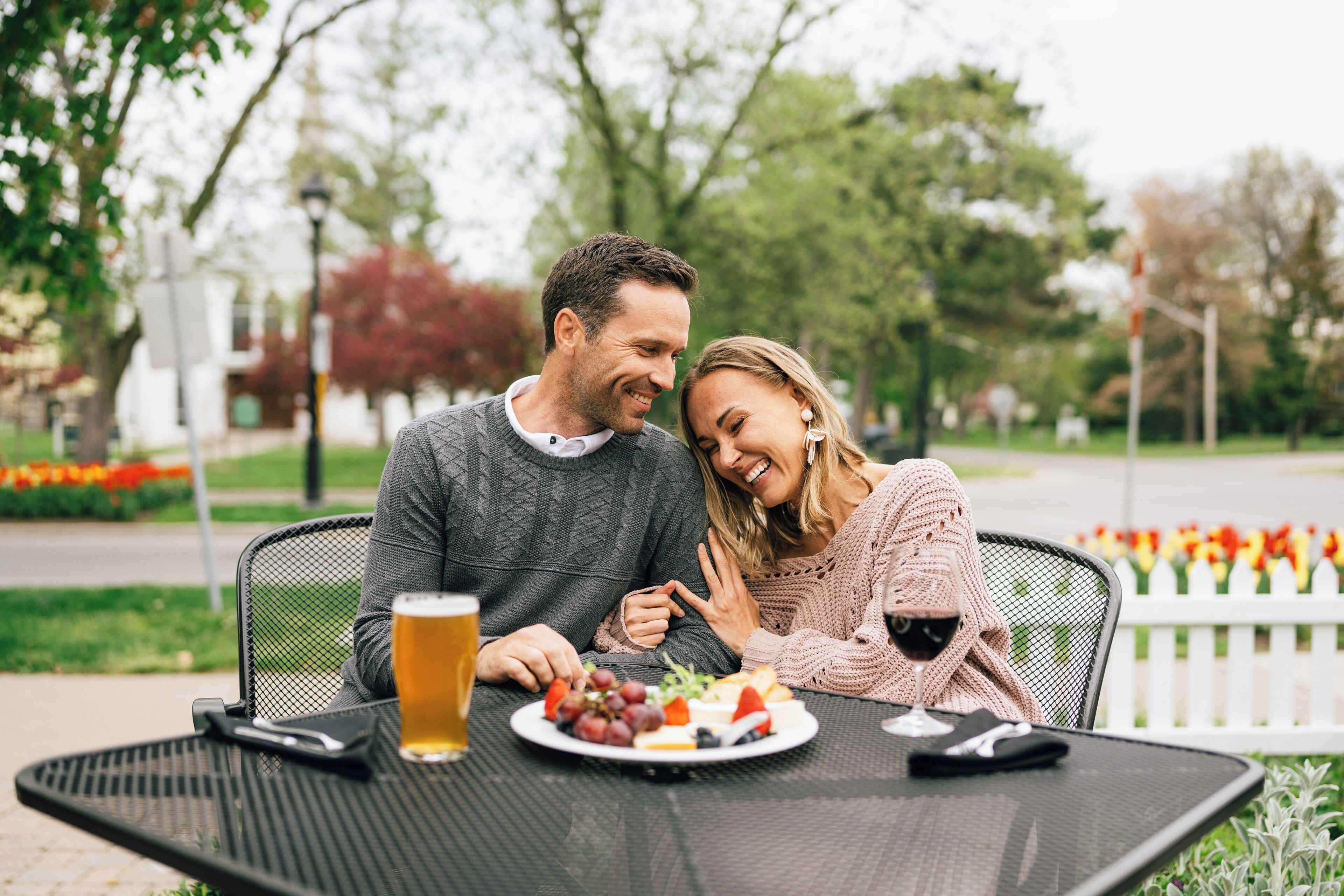 Una pareja cenando al aire libre en una mesa, con una cerveza, un plato de comida y un teléfono inteligente.